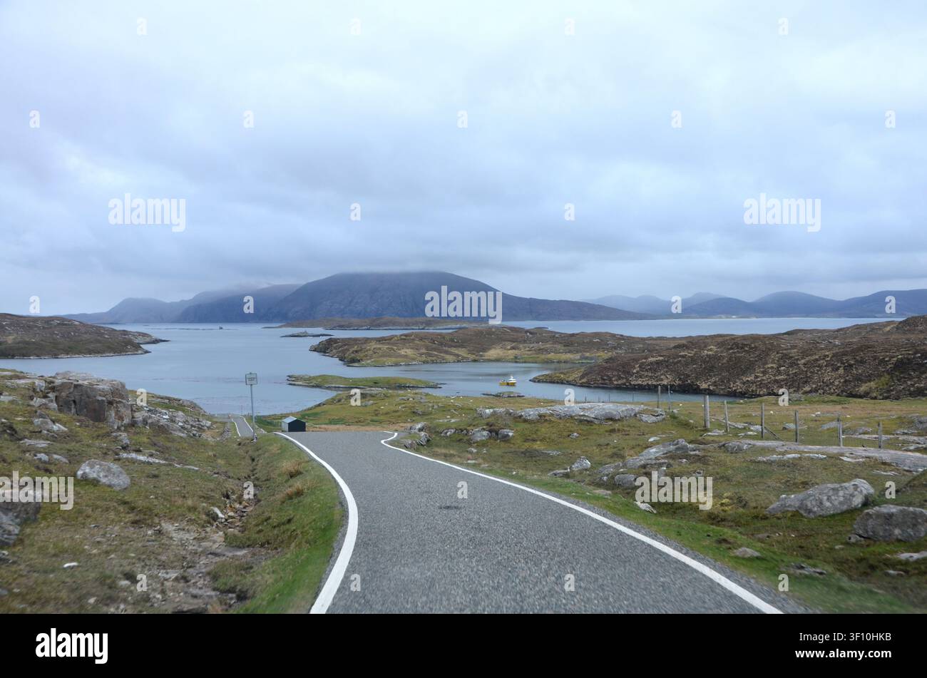Strada asfaltata deserta che porta verso un fiordo marittimo scenografico e montagne frastagliate nelle Highlands scozzesi, Scozia, Regno Unito Foto Stock