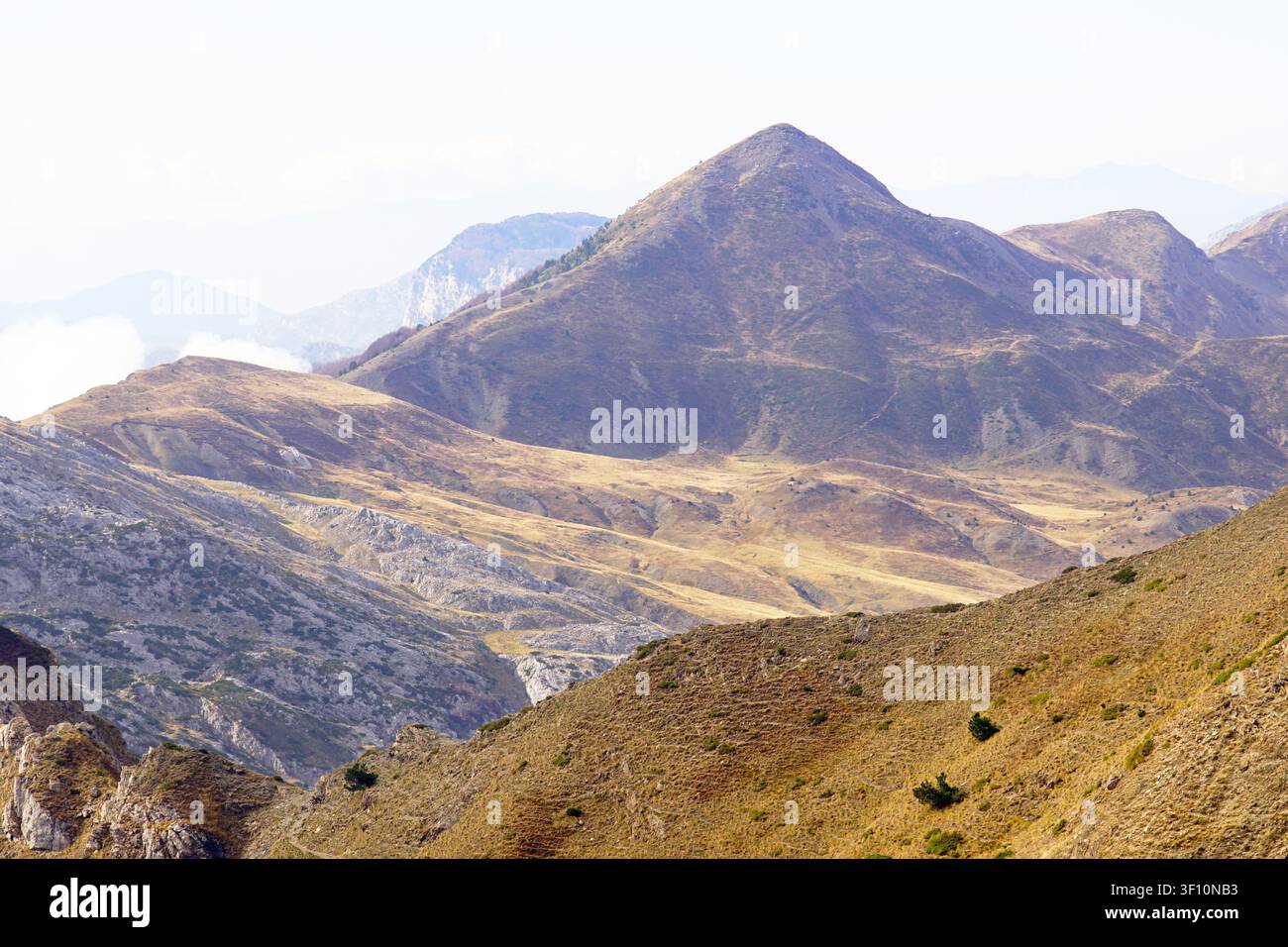 Dossi erbosi dorati e cima a forma di piramide nelle Accursed Mountains durante l'autunno. Transizione paesaggistica stagionale e altipiani panoramici dei Balcani. Foto Stock