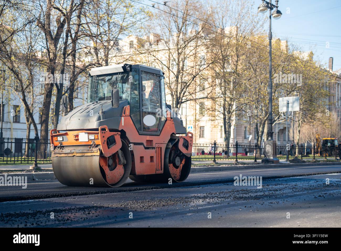 Il rullo stradale su strada compatte l'asfalto appena steso su strada, lavori di costruzione in città. Foto Stock