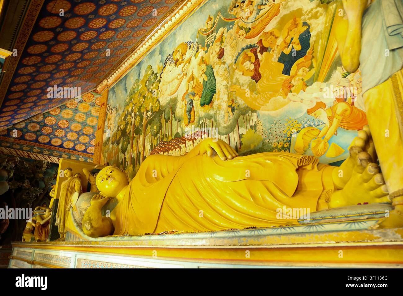 Grande statua di Buddha sdraiato in oro con vivaci murales tradizionali delle storie Jataka sul muro all'interno del tempio di Wewurukannala, Sri Lanka Foto Stock