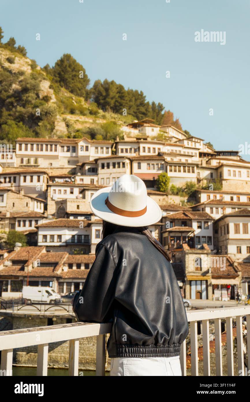 Vista posteriore di una donna in giacca di pelle appoggiata su un famoso ponte sospeso a Berat, Albania. Destinazione da visitare - Città delle mille finestre. Patrimonio mondiale UNESCO Foto Stock