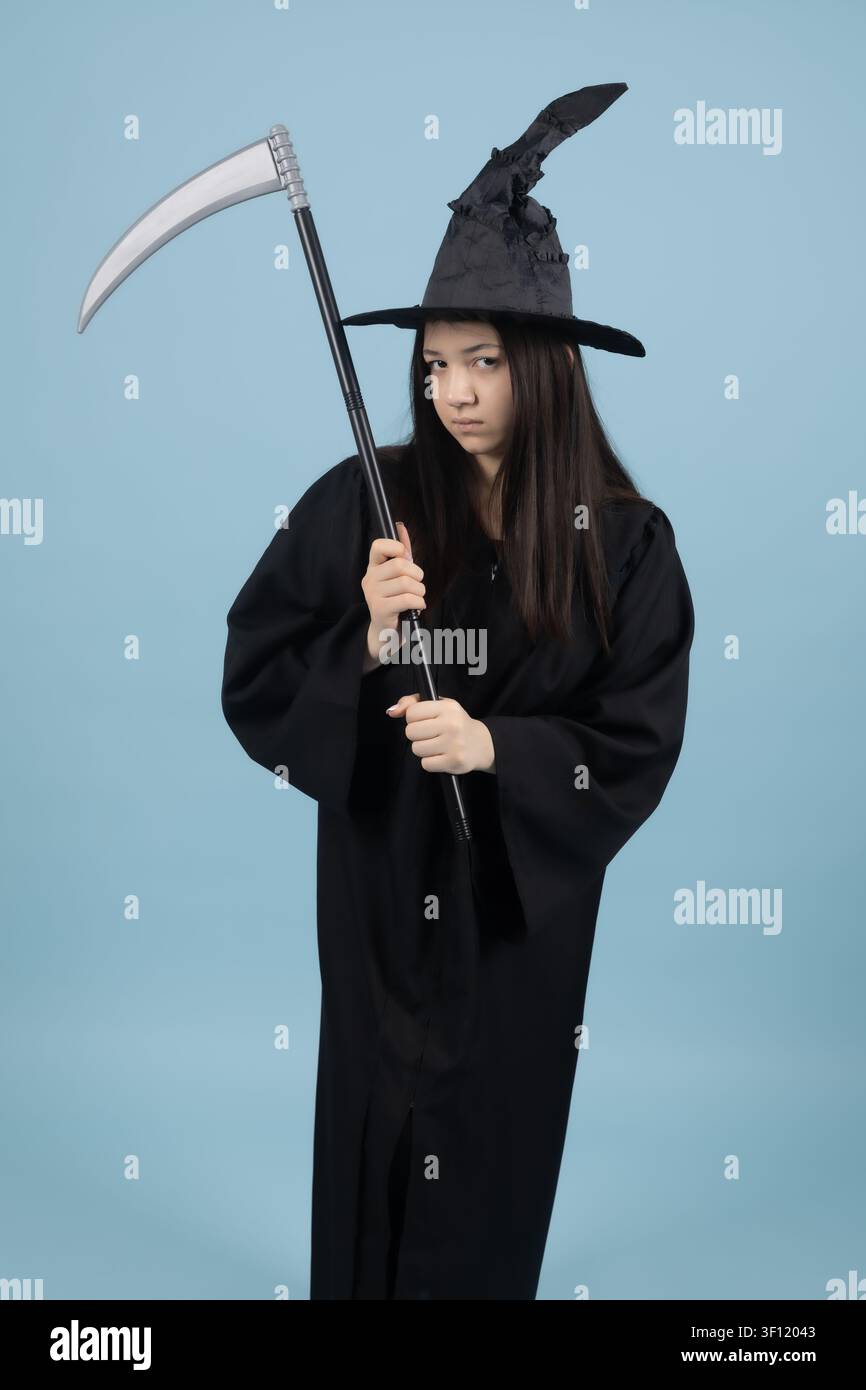 Giovane donna spaventosa in costume da strega che tiene una falce per Halloween Foto Stock