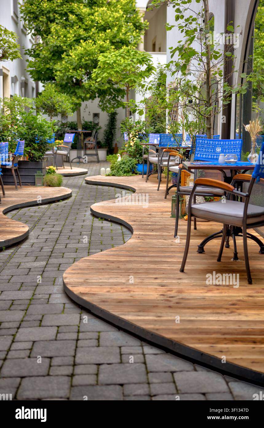 Sedili in legno curvi e tavoli da esterno in un cortile frondoso a Bratislava, Slovacchia. Foto Stock