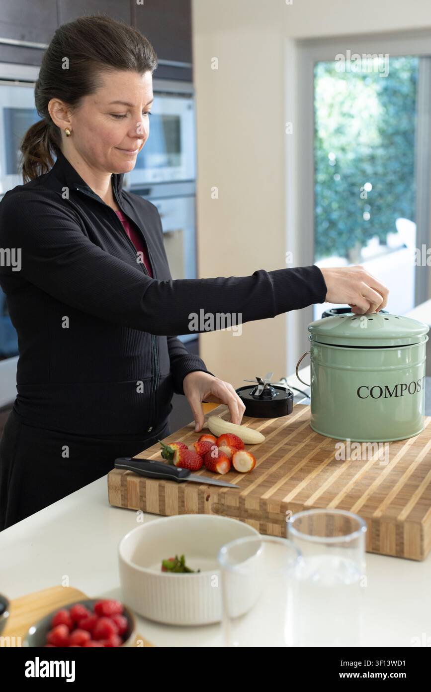 Donna con giacca nera con cerniera che taglia fragole su un tagliere di legno vicino a COMPOST Foto Stock