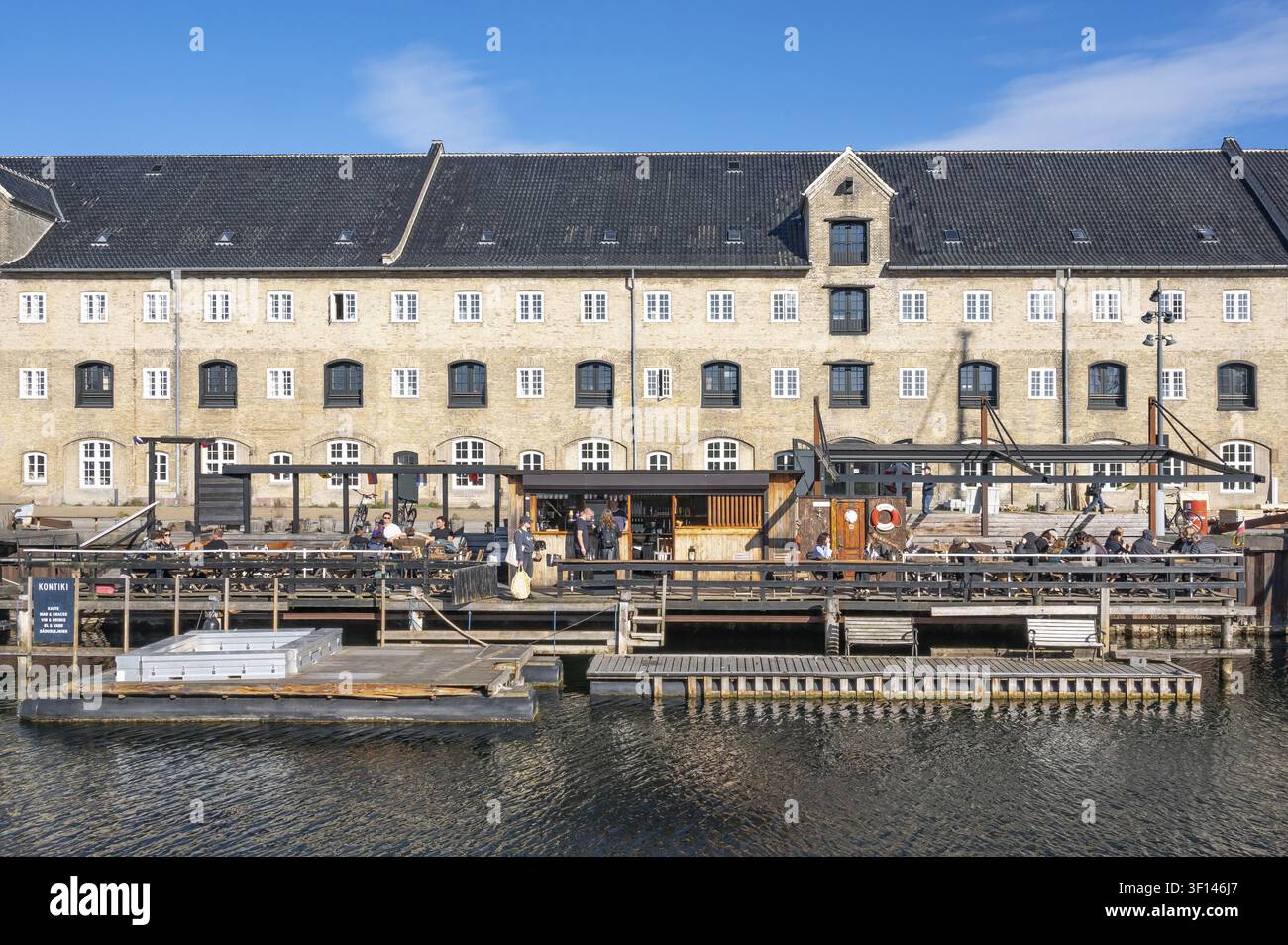 Gli ospiti siedono sulle terrazze in legno di una piattaforma di catering galleggiante con passaggi pedonali nel canale proprio di fronte alla facciata monumentale in mattoni di un histo Foto Stock