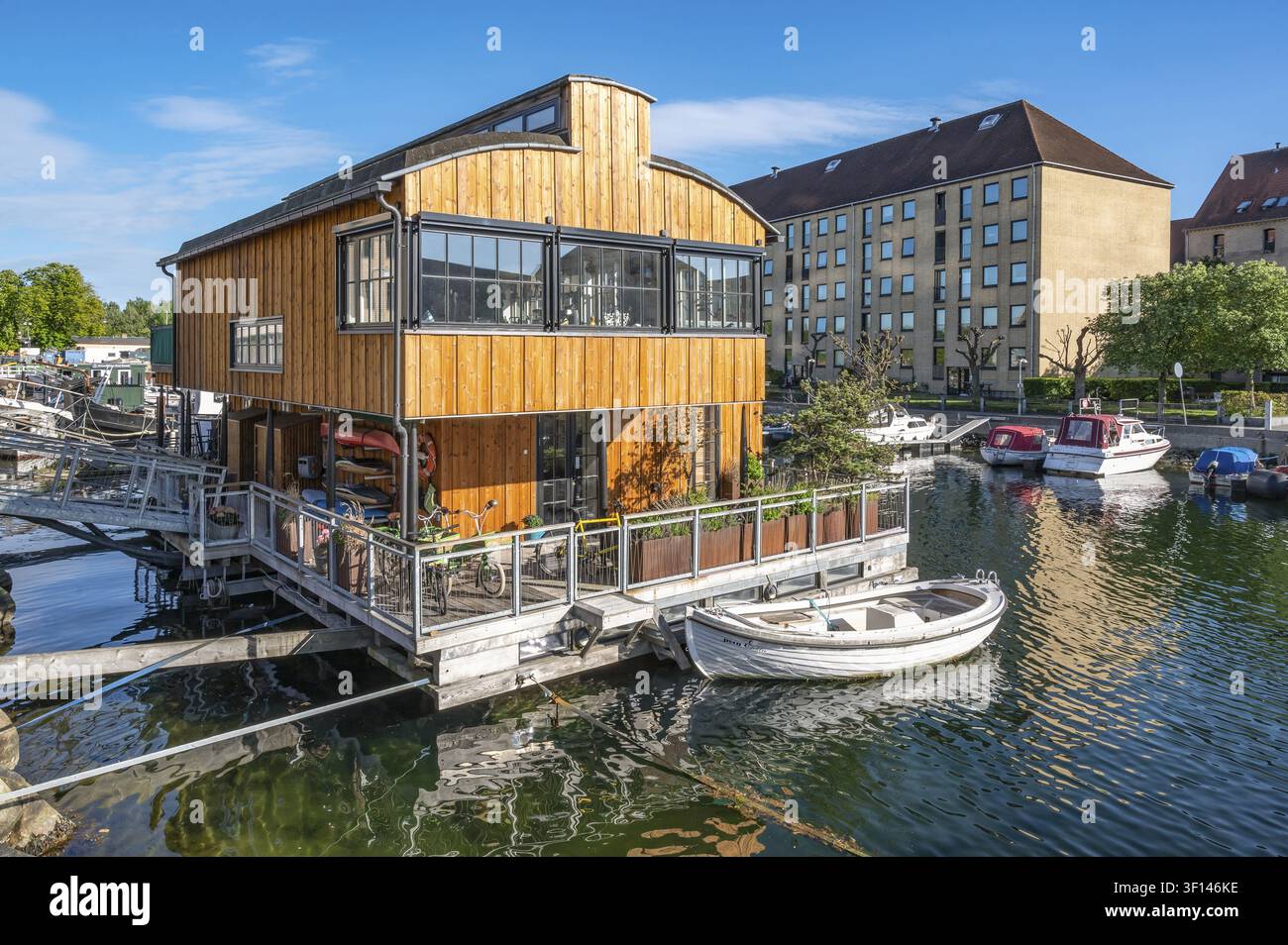 Una vista di una moderna casa galleggiante a due piani con un rivestimento in legno sorprendente, grandi finestre e un ponte in legno avvolgente, con una barca a remi ormeggiata nel Trangr Foto Stock