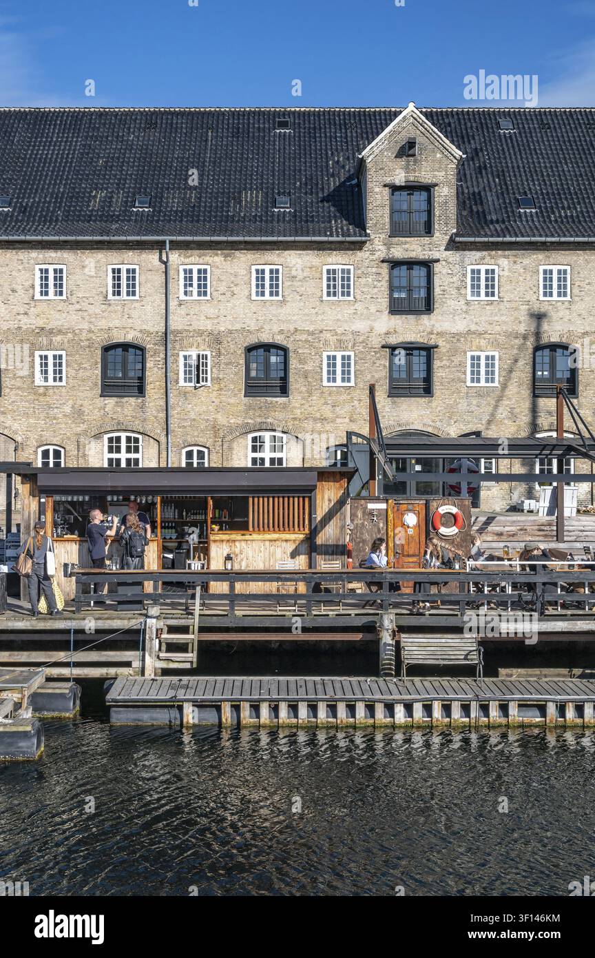 Gli ospiti siedono sulle terrazze in legno di una piattaforma di catering galleggiante con passaggi pedonali nel canale proprio di fronte alla facciata monumentale in mattoni di un histo Foto Stock
