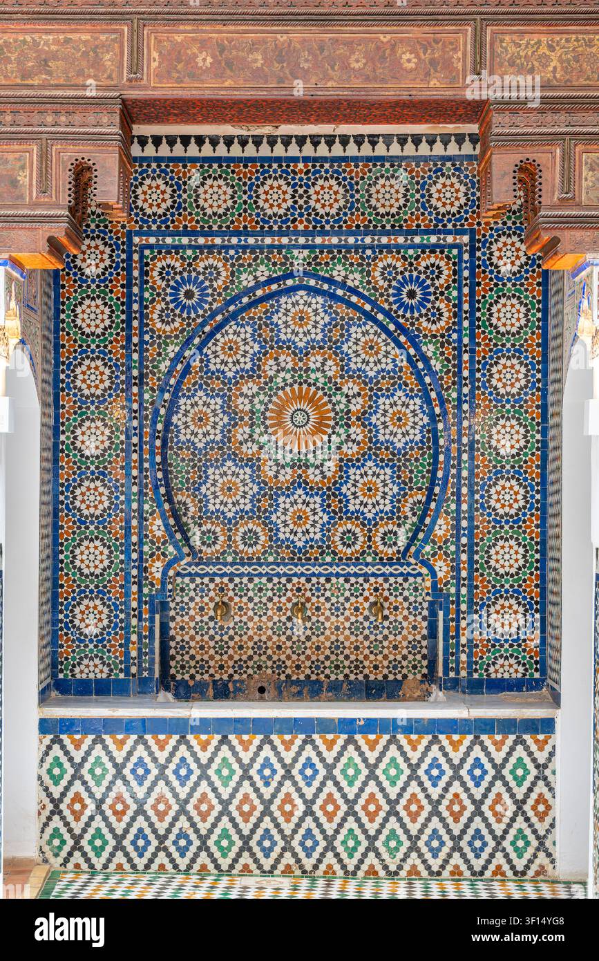 Una nicchia fontana murale decorativa a Dar Jamai ha un arco a ferro di cavallo che incornicia una superficie a mosaico zellige con motivi geometrici blu e verdi sopra un piccolo Foto Stock