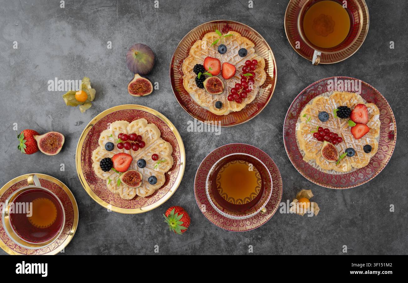 Disposizione in vista dall'alto di waffle pancake con frutti di bosco, fichi e tazze di tè su uno sfondo rustico Foto Stock