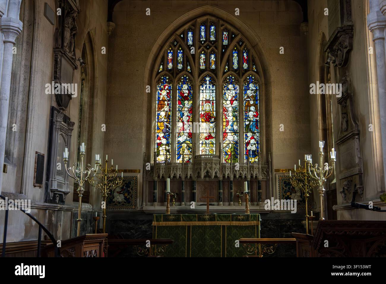 Vista interna della chiesa Holy Cross di Seend con una vetrata artistica sopra l'altare e candelabri religiosi Foto Stock