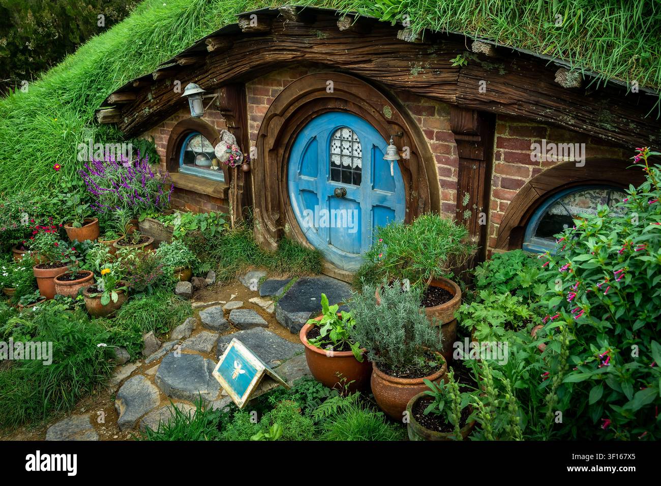Affascinante porta rotonda blu di una tana di hobbit incastonata nelle rigogliose colline verdi del set cinematografico di Hobbiton. Foto Stock