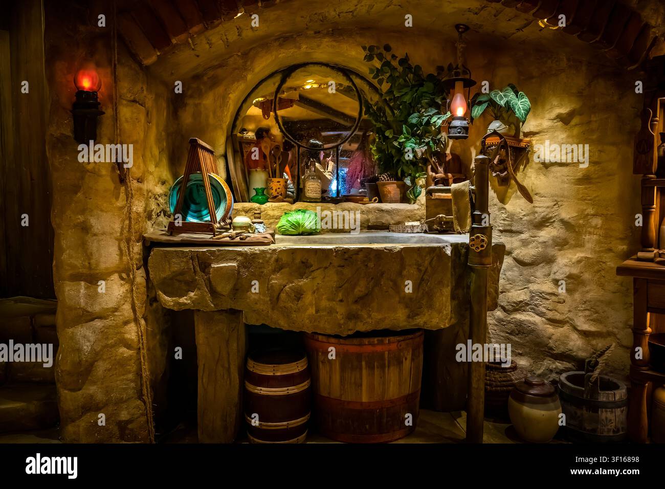 Un lavandino in pietra rustico all'interno di una cucina accogliente in stile Hobbit hole al set cinematografico di Hobbiton, con barili di legno vintage, ceramiche, uno specchio rotondo. Foto Stock