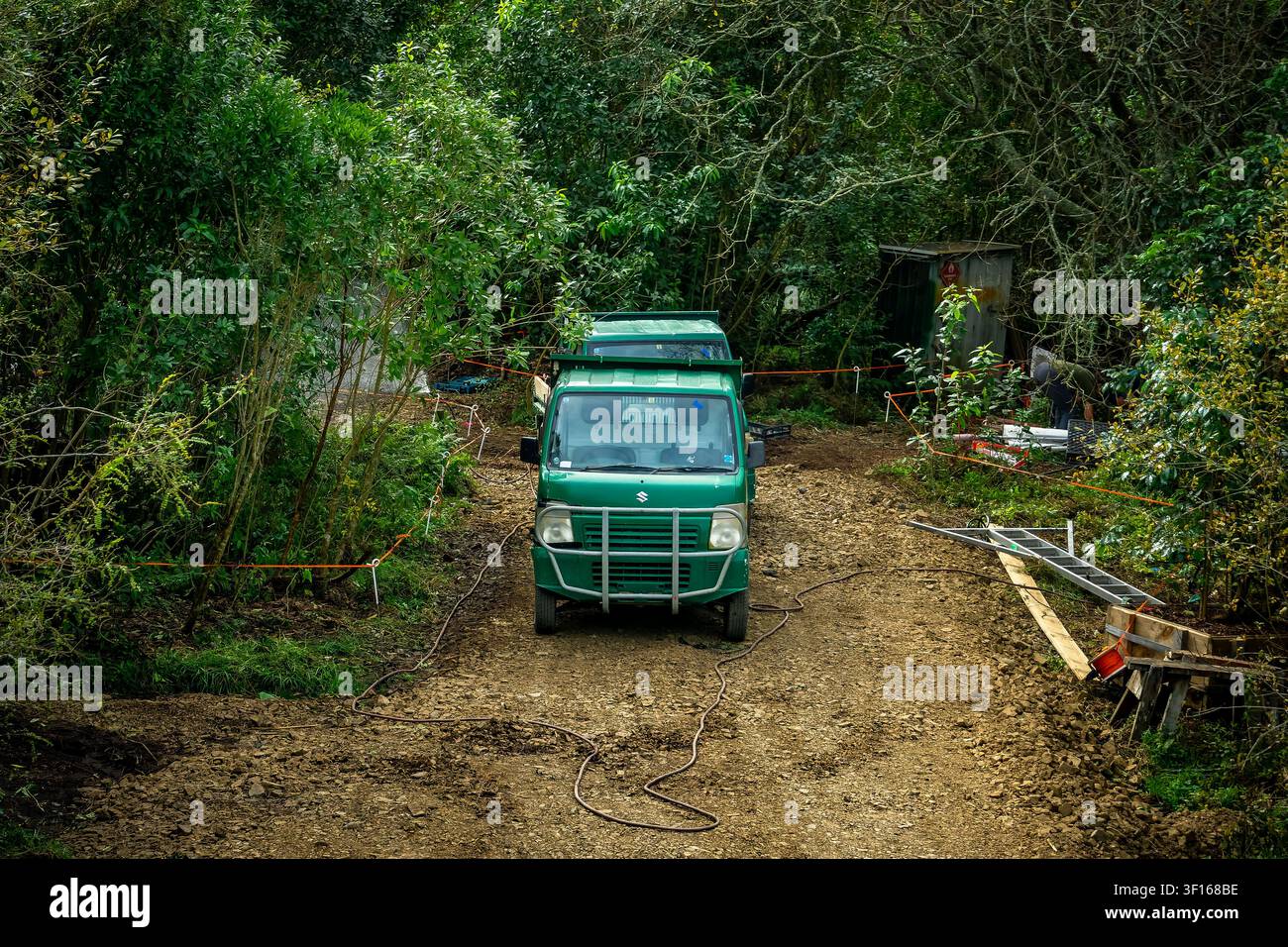 Un camioncino micro utilitario verde Suzuki è parcheggiato su un sentiero di servizio fangoso e non asfaltato in mezzo alla fitta vegetazione forestale durante la manutenzione in corso. Foto Stock
