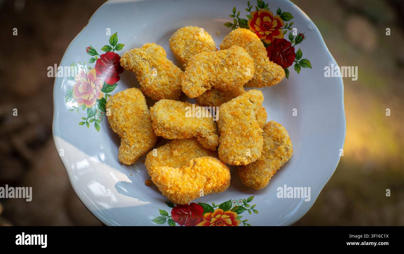 Nuggets di pollo croccanti serviti su un piatto bianco con fiori Foto Stock