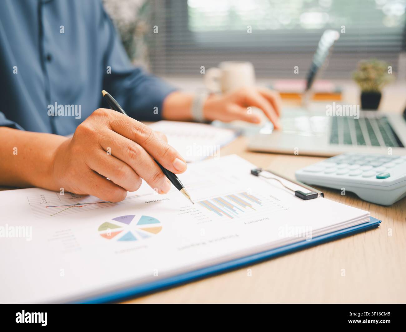 Prima piano di una mano che indica grafici finanziari colorati con calcolatrice e laptop sulla scrivania dell'ufficio, rappresentanti contabilità, revisione dei dati, analisi del budget, Foto Stock