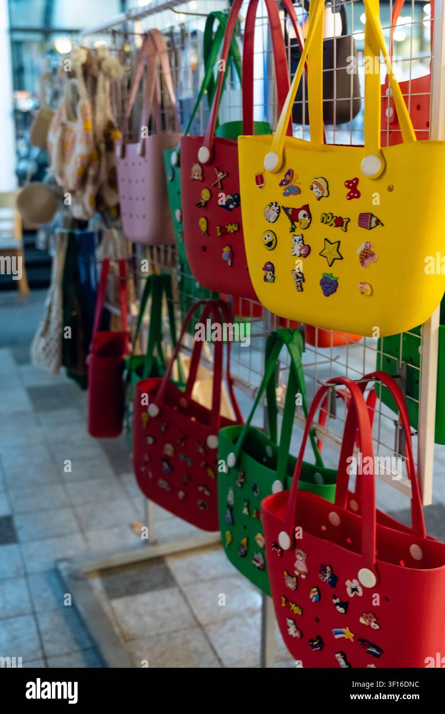 Borse di gomma colorate decorate con ciondoli giocosi appese ordinatamente su uno scaffale espositivo del mercato Foto Stock
