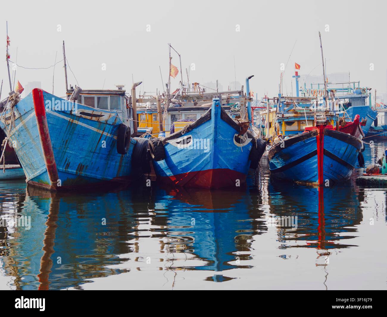 Coloratissimi barche da pesca in legno blu ormeggiate in un porto affollato a Da Nang, Vietnam, con riflessi nell'acqua calma. Foto Stock