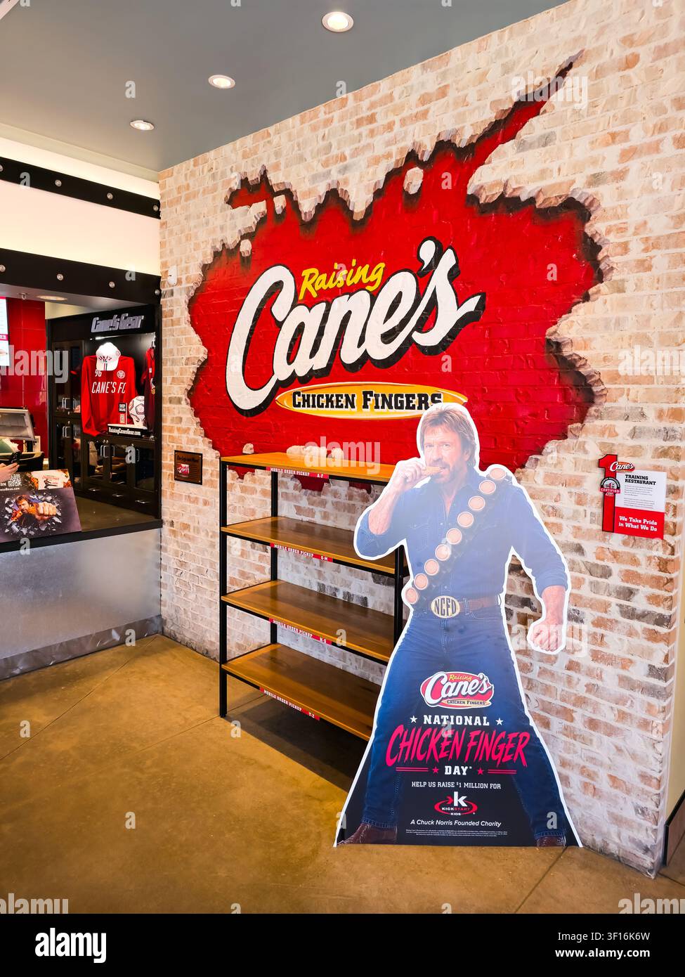DALLAS, TX, USA - 10 LUGLIO 2026: Interno di Raising Cane's Chicken Fingers con un muro espositivo prominente con logo e un ritaglio di cartone a tema Foto Stock