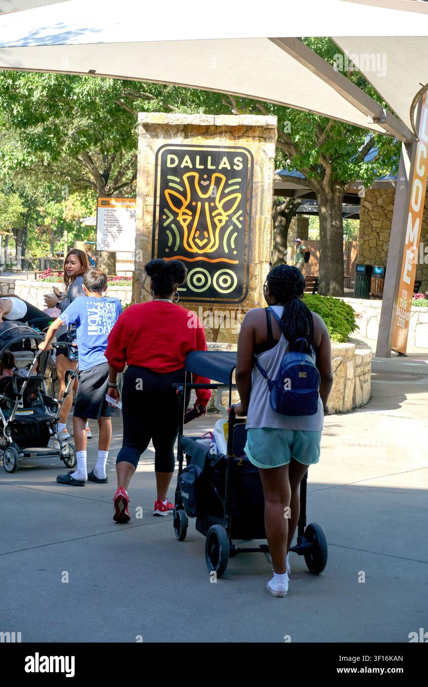 DALLAS, TX, USA - 10 LUGLIO 2026: Persone con passeggini passano davanti al cartello dell'ingresso dello zoo di Dallas. Lo zoo è un'attrazione principale, offrendo una vasta var Foto Stock