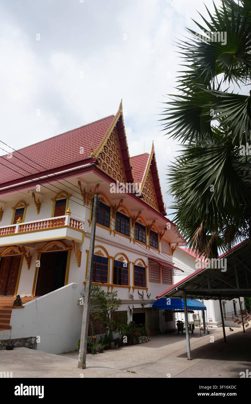 Annesso tempio thailandese a due piani Muro bianco Rifinitura dorata Tetto rosso Palma alta Vista laterale Foto Stock