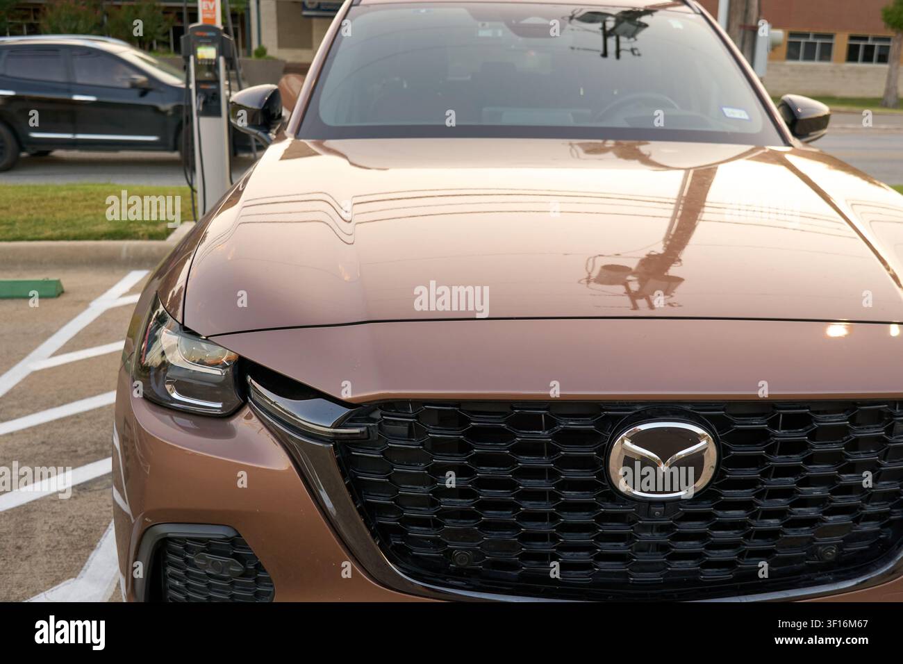 FARMERS BRANCH, TX, USA - 10 LUGLIO 2026: Mazda CX-70 PHEV in Melting Copper Metallic è parcheggiato a una stazione di ricarica, mostrando la sua elegante griglia frontale Foto Stock