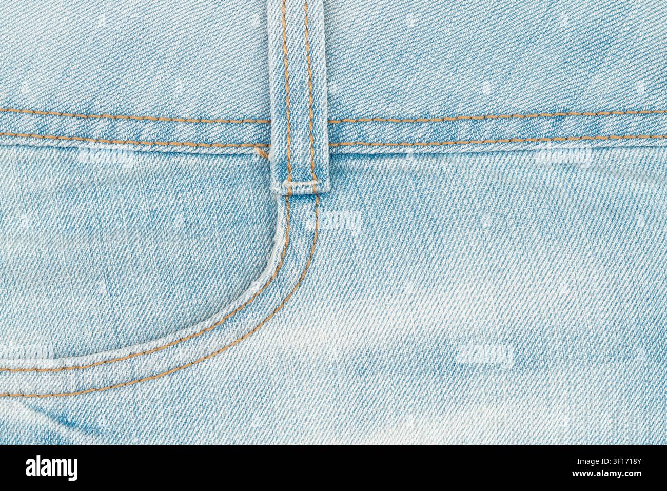 Dettaglio macro di tessuto denim blu chiaro. Mostra la tasca anteriore, l'asola per la cintura e le doppie cuciture con filo arancione. Sfondo piatto e pulito per tessuti Foto Stock