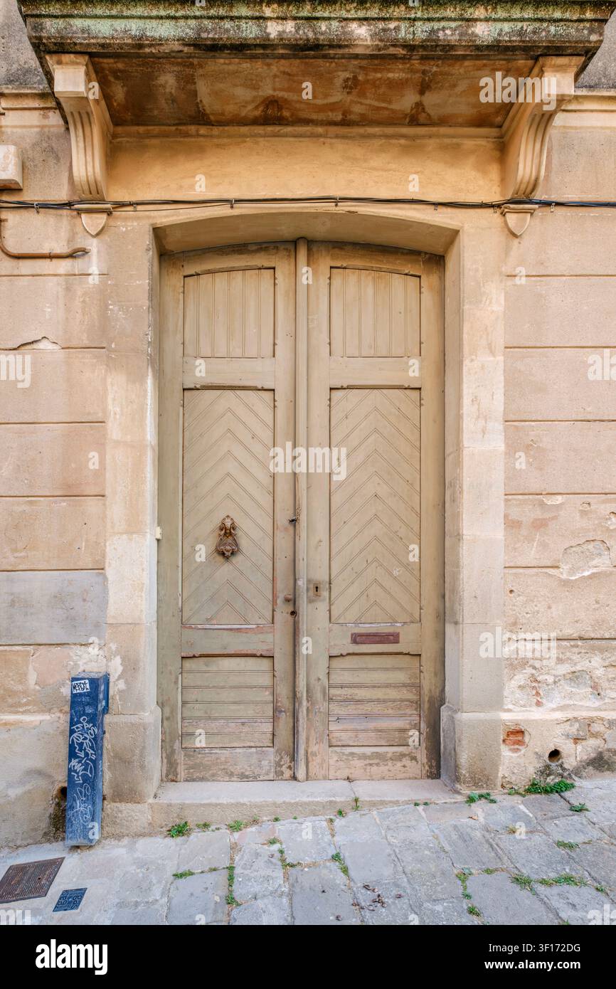 Antica porta doppia in legno rustico e battente in ottone antico nella facciata di un edificio in pietra Foto Stock