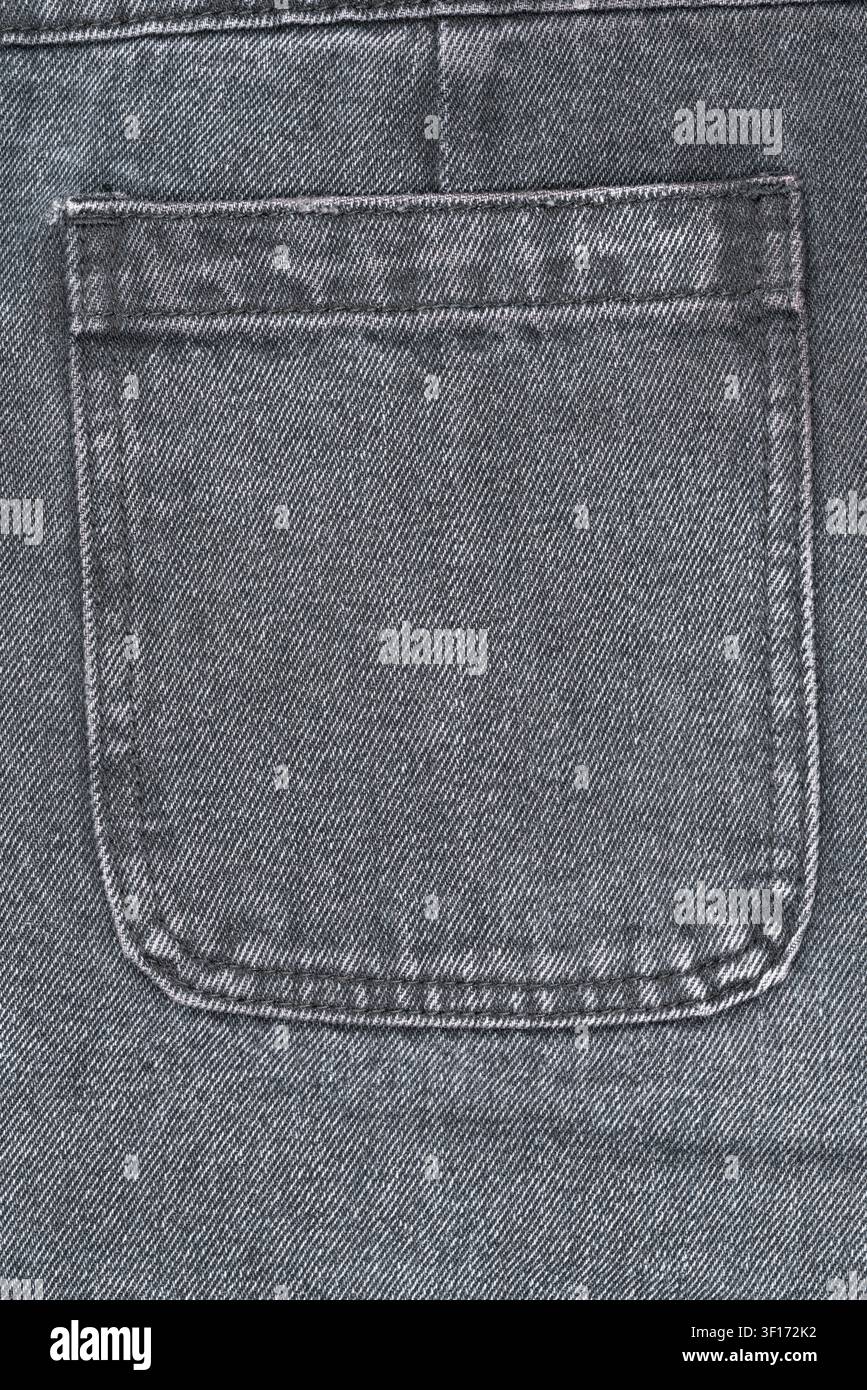 Scatto macro dettagliato della tasca posteriore di jeans neri sbiaditi. Mostra la classica cucitura del tessuto denim. Toni grigi neutri creano uno sfondo versatile per Fas Foto Stock