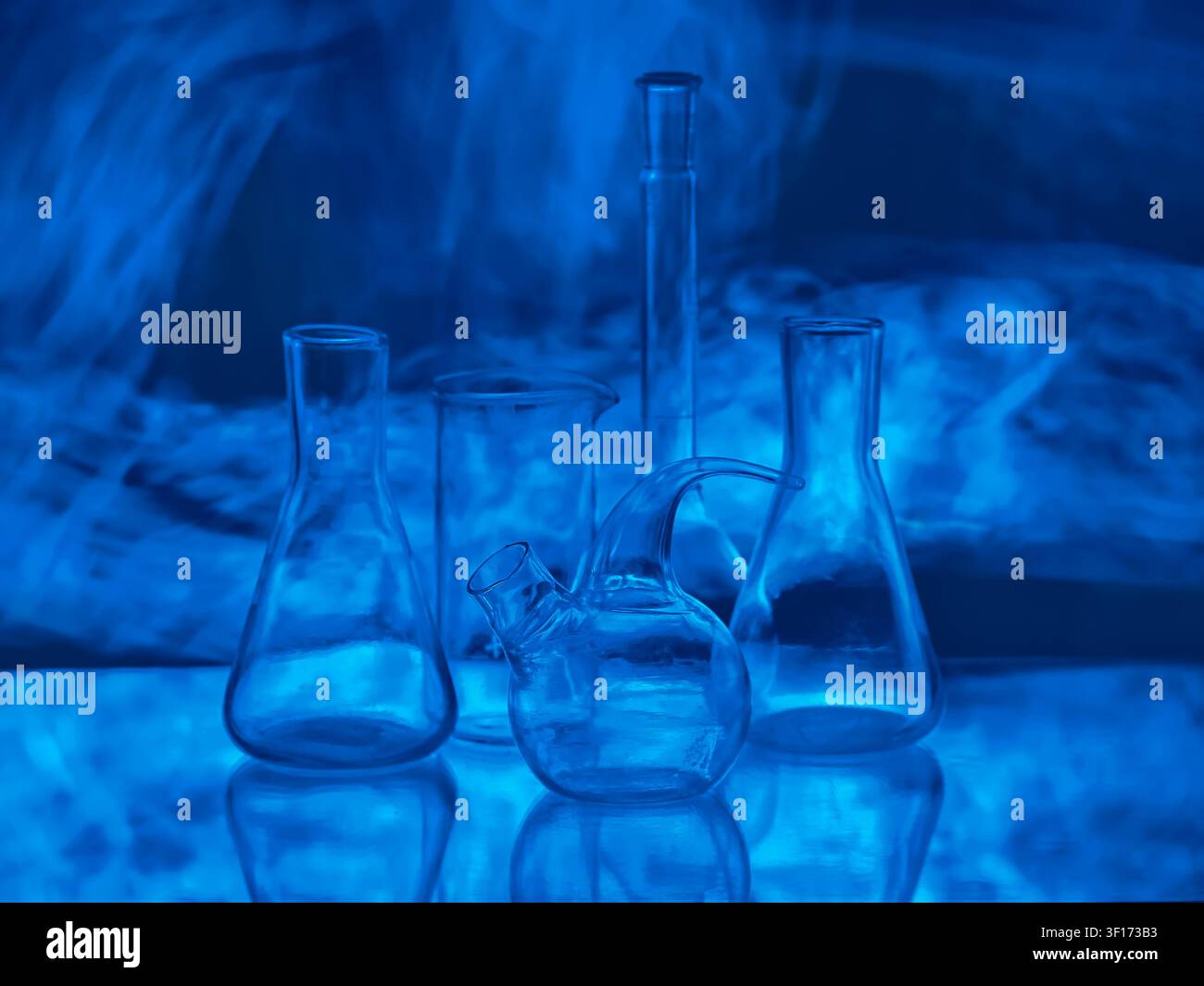 Fiaschi da laboratorio di vetro vuoti e retorti nella luce al neon blu scuro con fumo misterioso per la ricerca scientifica, la biotecnologia, l'innovazione medica e Foto Stock