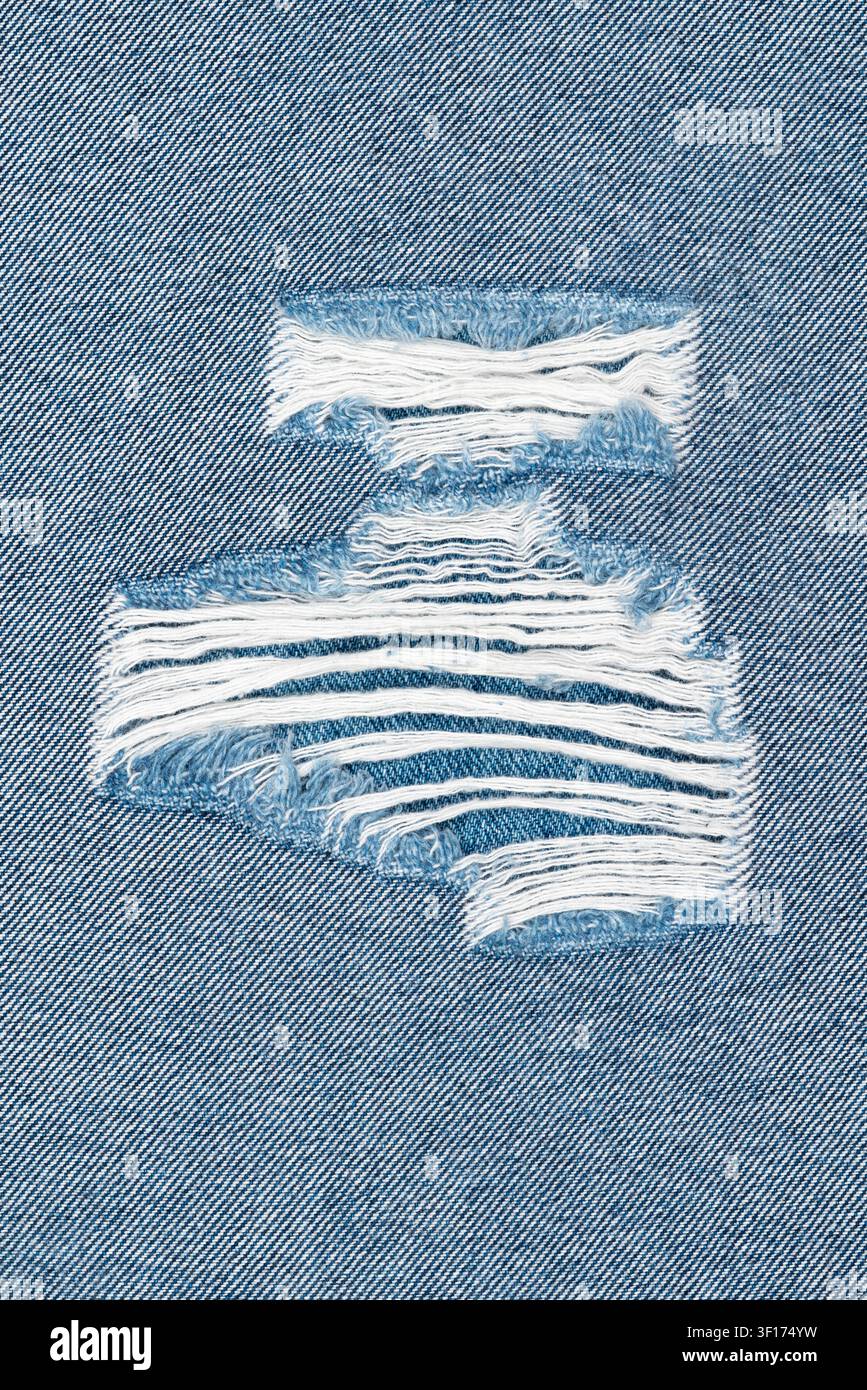 Prima vista di denim distrutto con strappi orizzontali che rivelano fili bianchi sottostanti. La trama di cotone blu domina. Una luce naturale soffusa mette in risalto Foto Stock