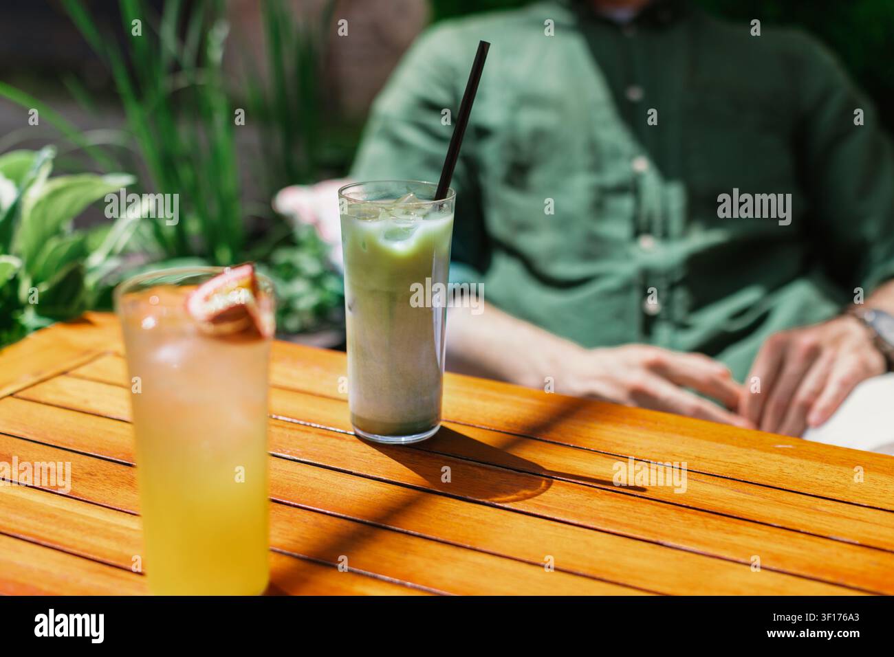Primo piano di un uomo seduto a un tavolo da caffè in una giornata estiva con un latte matcha freddo Foto Stock