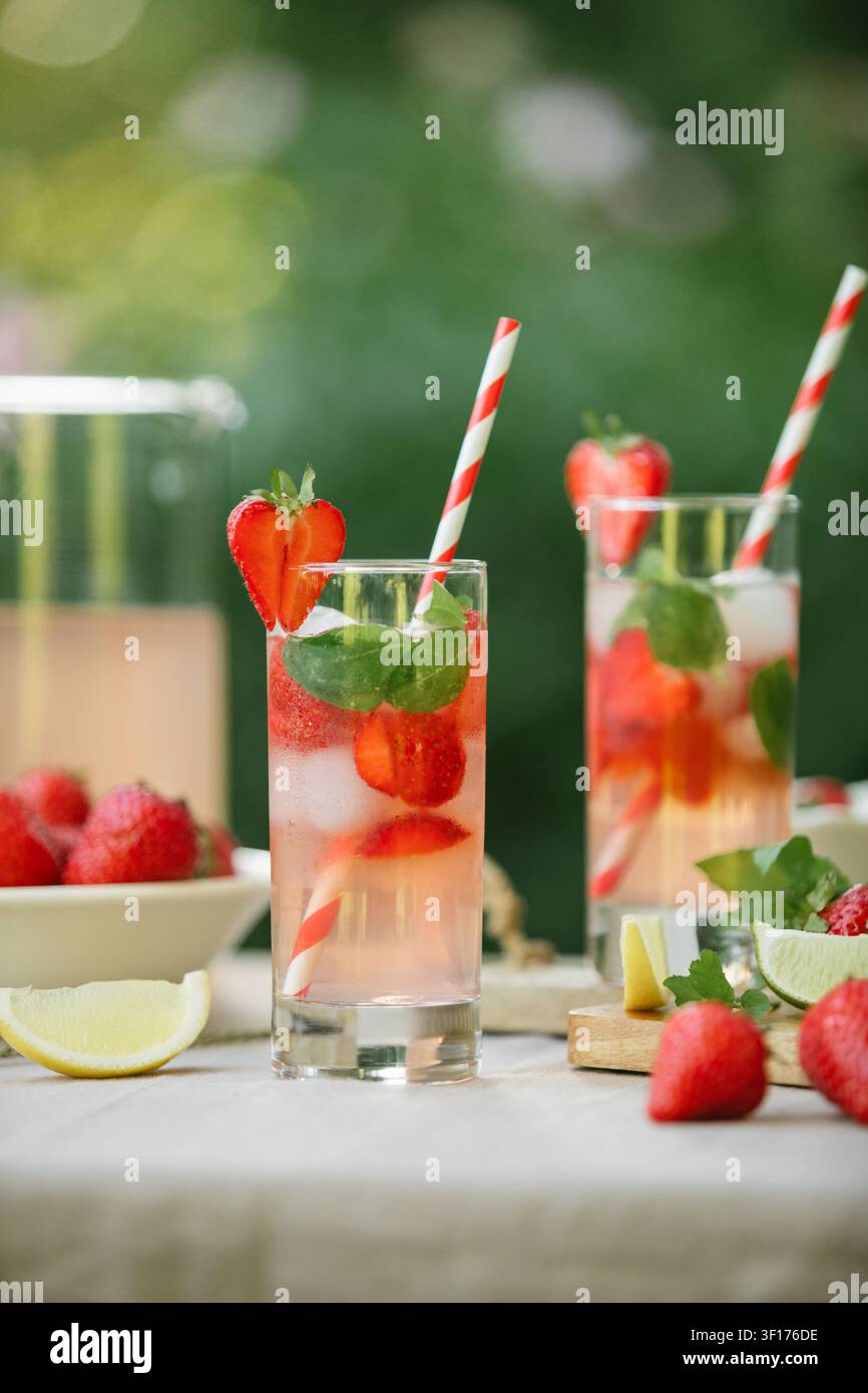Primo piano di una brocca e due bicchieri di limonata alla fragola fatta in casa con menta fresca su un tavolo da giardino in una giornata estiva soleggiata Foto Stock