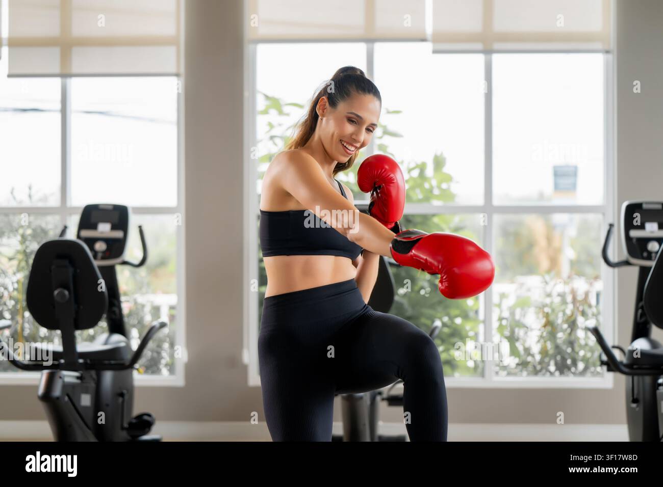 Giovane donna sicura di sé con guantoni da boxe rossi che si diverte con l'allenamento di boxe e il lavoro di piedi in palestra. Scena per coaching personale, viaggio di perdita di peso, quotidiano w Foto Stock