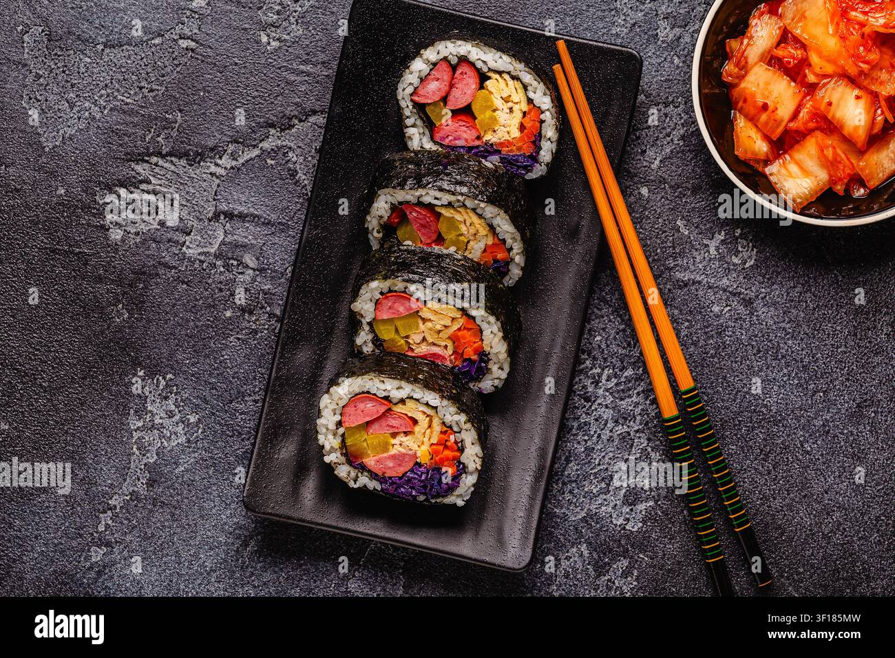 Un piatto nero pieno di kimbap (o gimbap) con ripieni colorati. Gli ingredienti includono salsiccia, cetrioli, uovo e verdure. Foto Stock