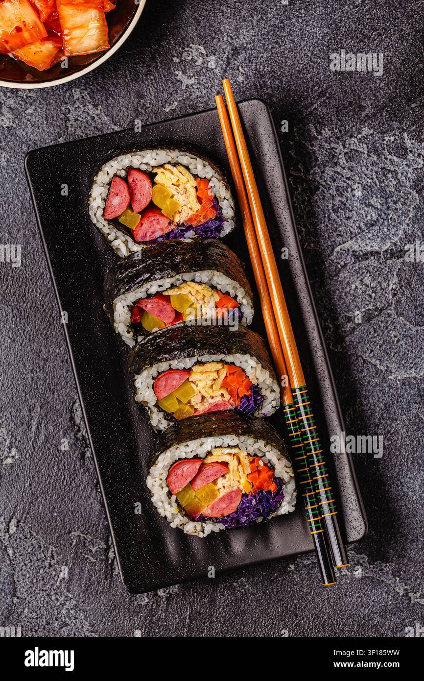 Un piatto nero pieno di kimbap (o gimbap) con ripieni colorati. Gli ingredienti includono salsiccia, cetrioli, uovo e verdure. Foto Stock