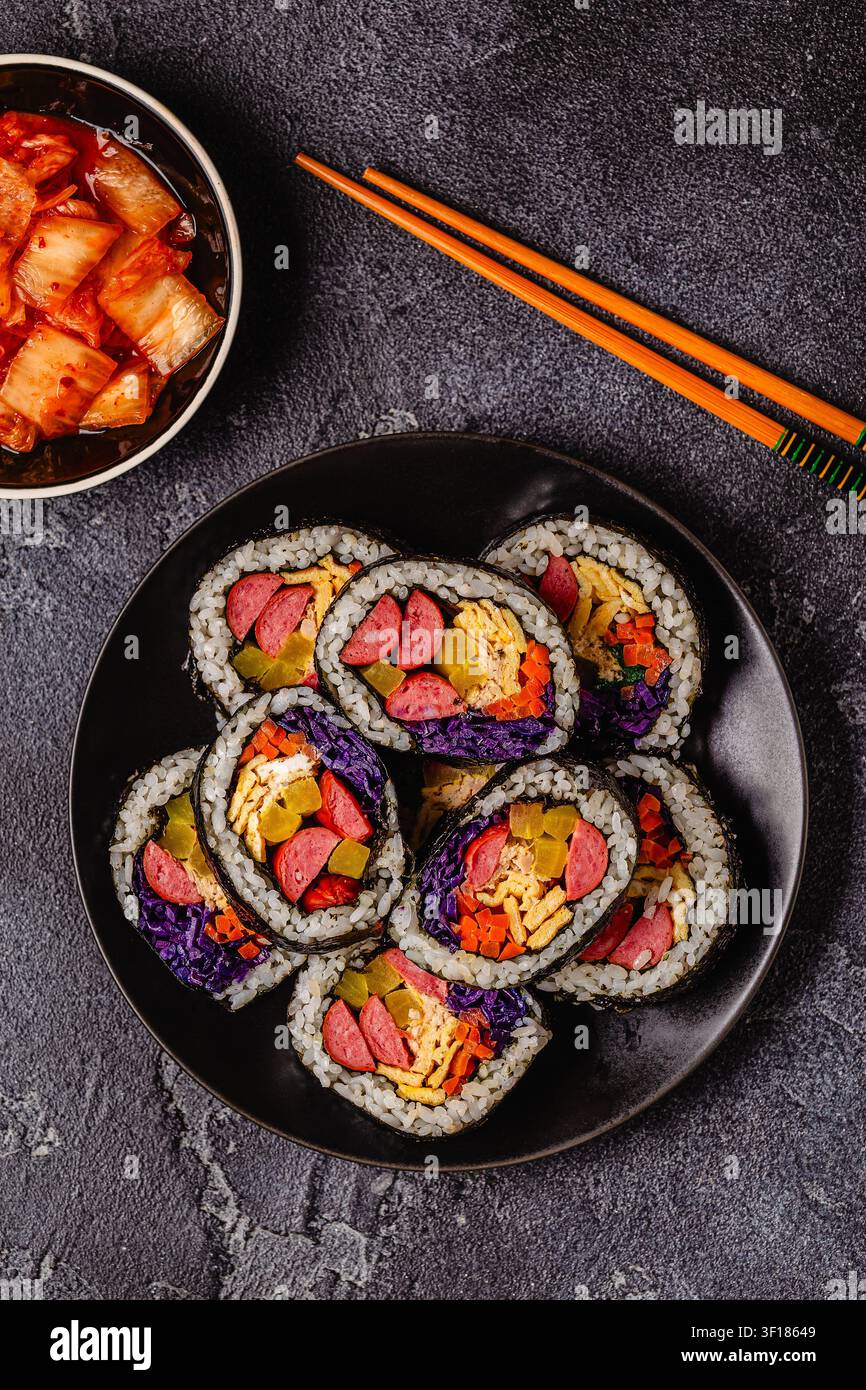 Un piatto nero pieno di kimbap (o gimbap) con ripieni colorati. Gli ingredienti includono salsiccia, cetrioli, uovo e verdure. Foto Stock
