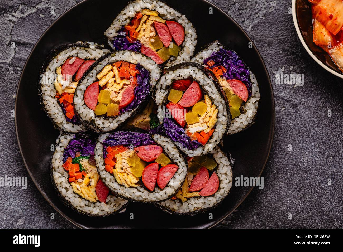 Un piatto nero pieno di kimbap (o gimbap) con ripieni colorati. Gli ingredienti includono salsiccia, cetrioli, uovo e verdure. Foto Stock