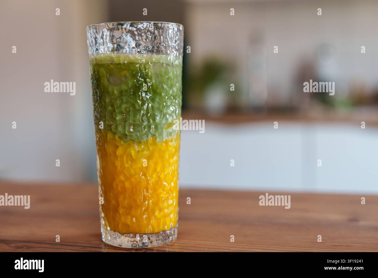 Latte matcha al mango ghiacciato a strati in un bicchiere alto sul tavolo della cucina Foto Stock