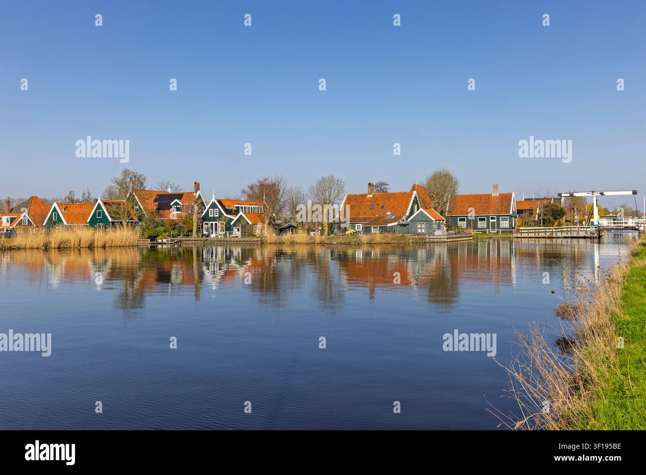 Zaandam, Paesi Bassi. Vista scenografica del museo all'aperto storico di Zaanse Schans con tradizionali case in legno verde e un ponte levatoio che si riflette nell'acqua Foto Stock