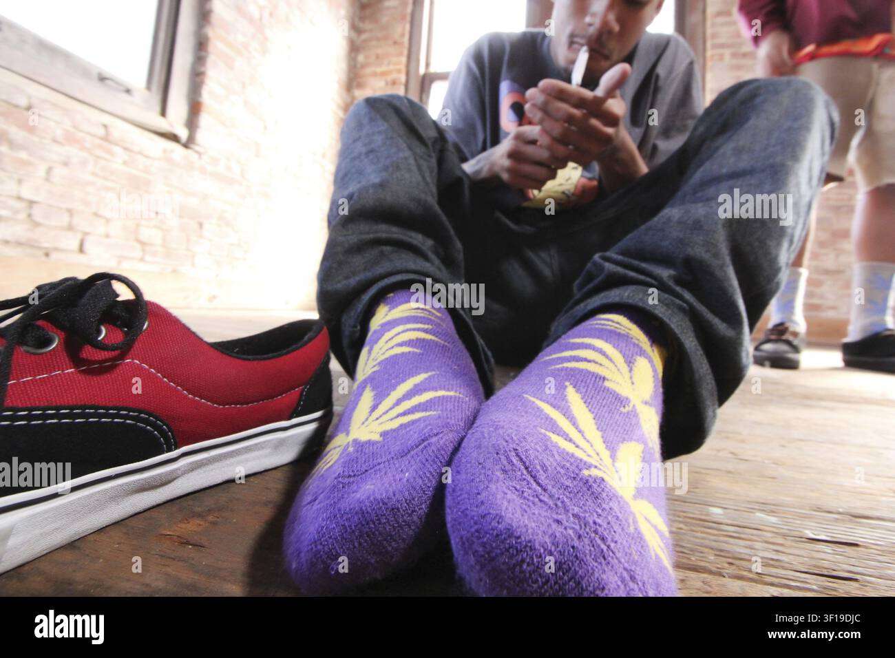 Primo piano di una persona seduta sul pavimento che indossa calzini viola con disegno di foglie, accanto a scarpe da ginnastica rosse, che evocano un'atmosfera casual e rilassata, Odd Future ra Foto Stock