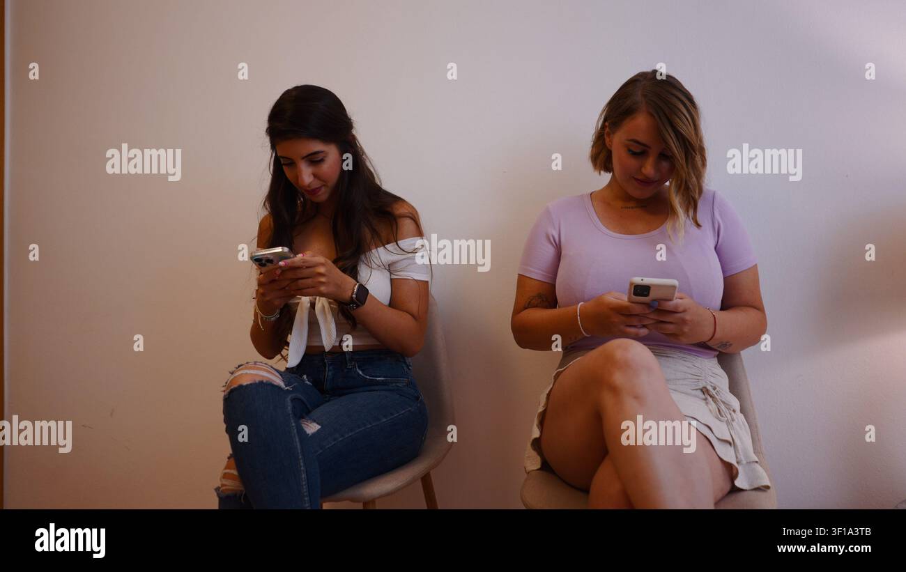 Giovani donne al telefono mentre aspettano nella reception di una clinica estetica Foto Stock