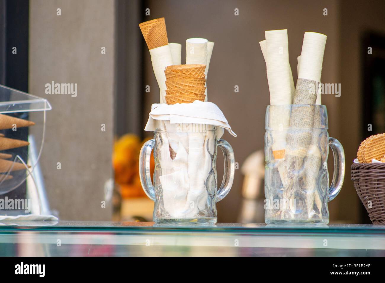 Coni di gelato con waffle e involucri di carta dentro grandi tazze di vetro sul bancone della gelateria. Foto Stock
