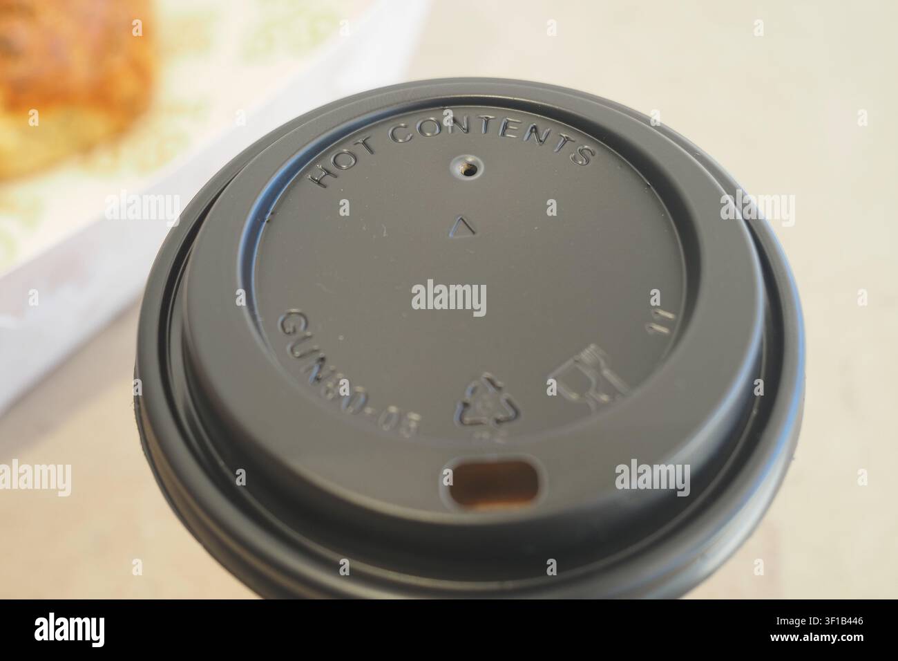Coperchio della tazza di caffè con simboli di avvertimento e riciclaggio in un caffè Foto Stock