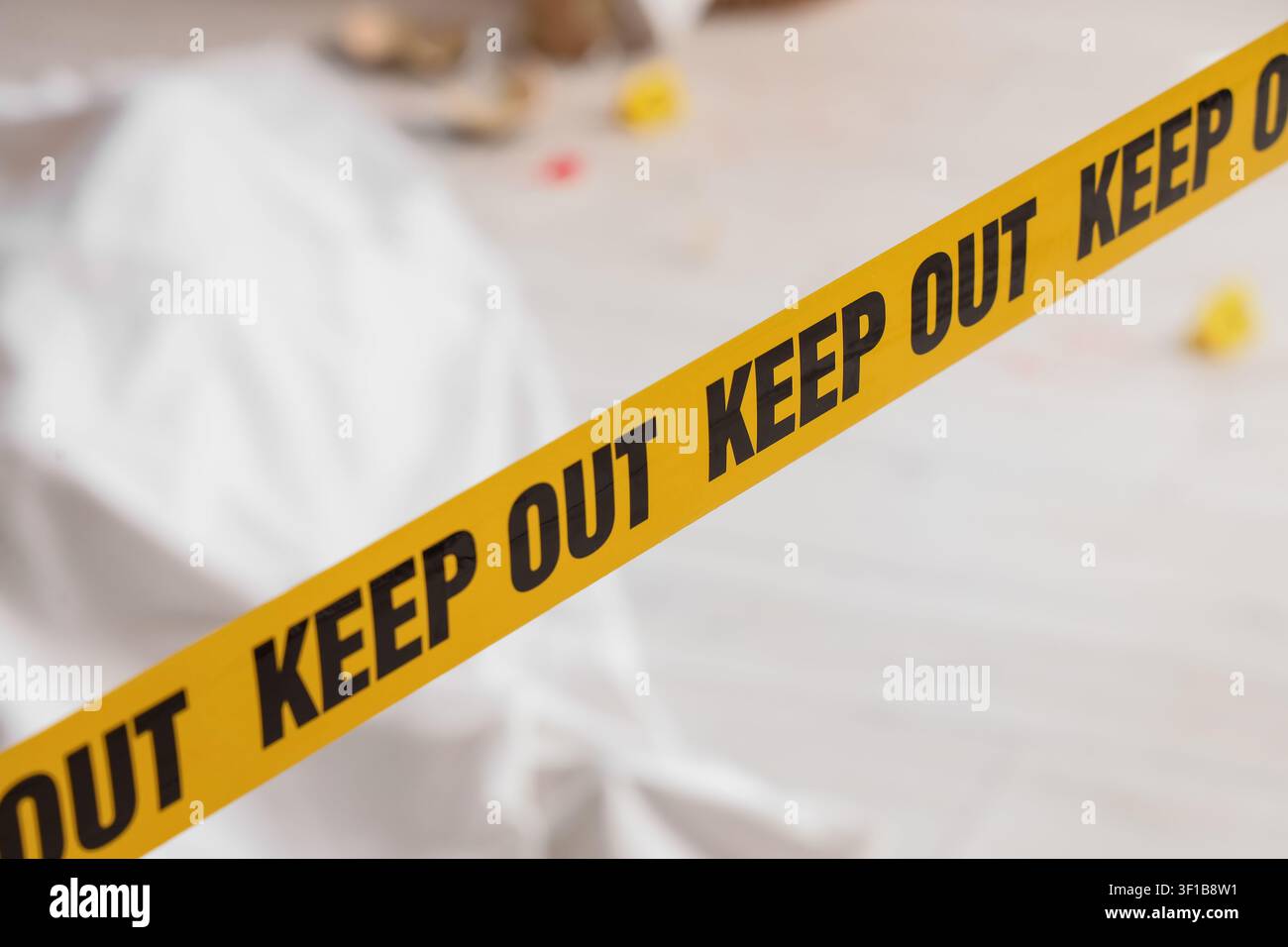 Nastro giallo di divieto di accesso su una scena del crimine con un corpo coperto da un lenzuolo bianco sullo sfondo Foto Stock