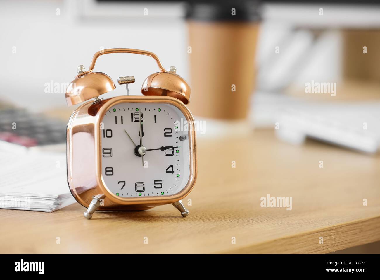 Sveglia in rame su una scrivania di legno con una tazza di caffè sfocata e documenti sullo sfondo, l'orologio ha un quadrante bianco con numeri neri chiari Foto Stock