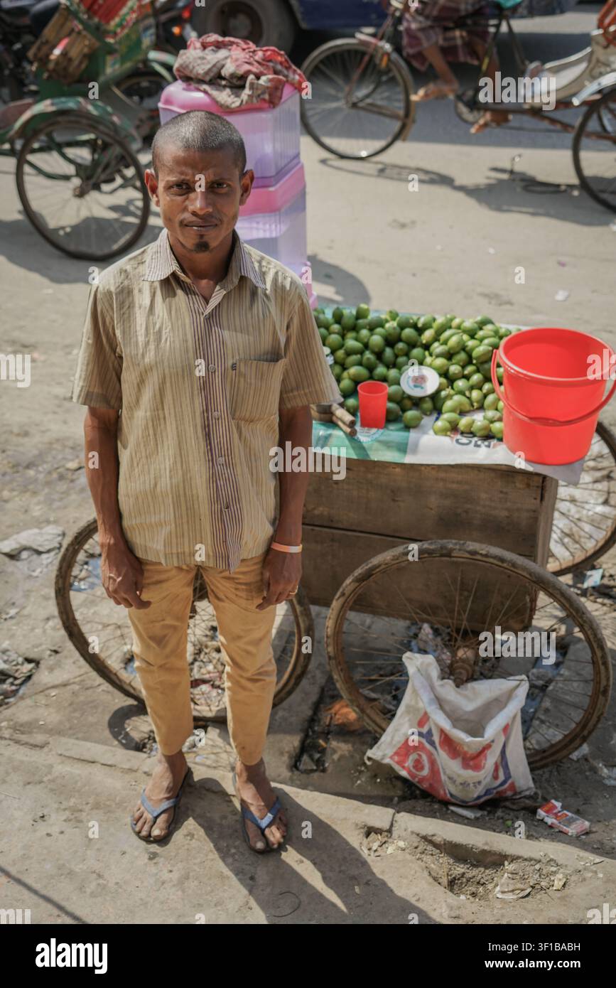 Dhaka, Bangladesh - 26 febbraio 2017: Un uomo con capelli corti e scuri, che indossa una camicia a maniche corte a righe e pantaloni marroni, si trova davanti a un'auto di legno Foto Stock