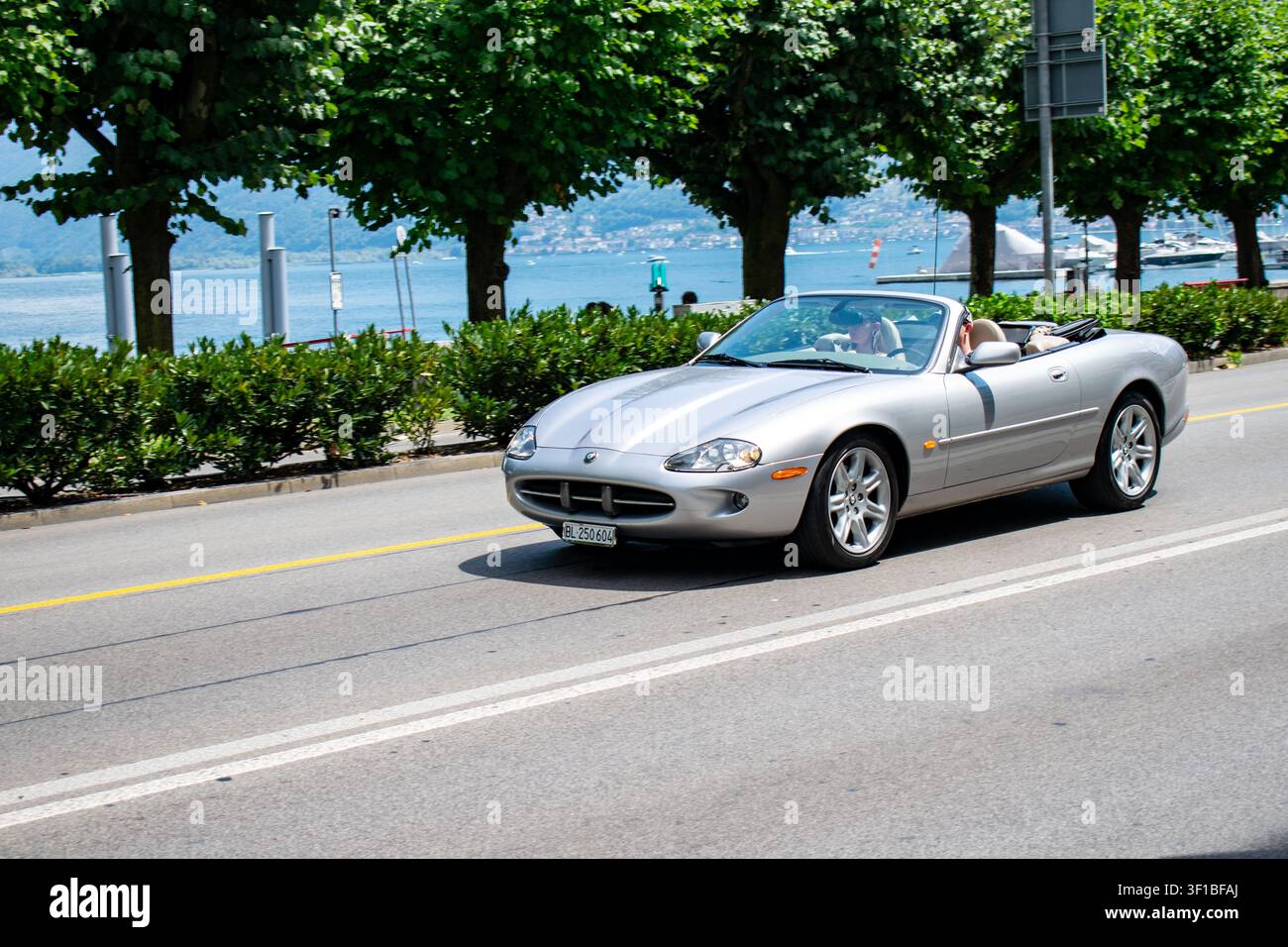Cabrio Jaguar XK8 argentato che percorre il lungolago del Lago Maggiore a Locarno, Ticino, Svizzera, in una giornata estiva soleggiata. Foto Stock