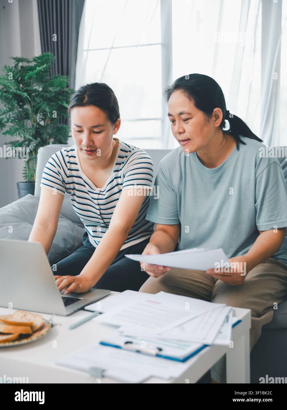 Madre asiatica e figlia adulta che utilizzano un laptop con documenti a casa, concetto di finanze familiari, pianificazione assicurativa, banche online, scartoffie e auto Foto Stock