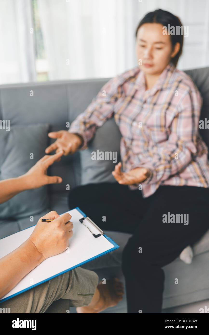 Cliente femminile spiega i suoi sentimenti con le mani aperte mentre il terapeuta prende appunti durante il counseling, mostrando la terapia del dialogo, l'ascolto attivo e il sostegno emotivo Foto Stock