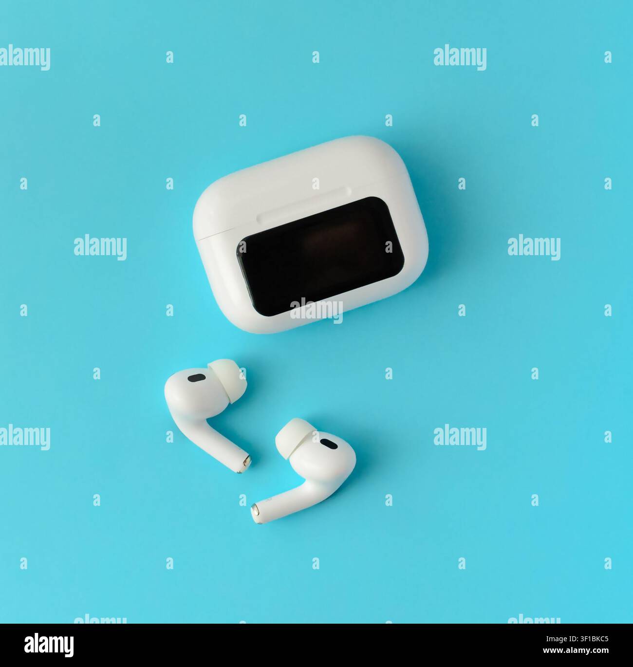 Auricolari wireless bianchi con custodia di ricarica chiusa su sfondo blu. Composizione tecnologica minima per musica, comunicazione e uso quotidiano Foto Stock